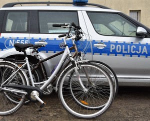 Zabezpieczone przez policję rowery. W tle oznakowany radiowóz.