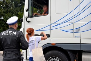 Policjant wraz z pracownikiem PKP wręczają kierowcy ulotki informacyjne.