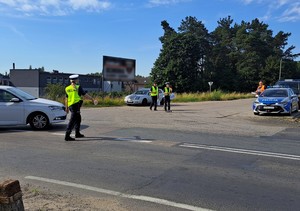 Policjantka stoi na ulicy dając kierowcy znak lizakiem nakazujący zatrzymanie pojazdu do kontroli drogowej.