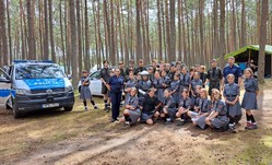 Zdjęcie grupowe z harcerzami w lesie. W pobliżu stoi radiowóz.