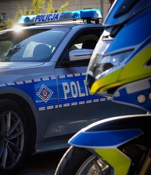 Bok radiowozu i przód policyjnego motocykla w nowych barwach oznakowania.