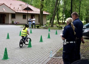 Dziecko jedzie na rowerze pod okiem policjantów.