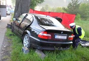 Policjant przy rozbitym aucie sporządza oględziny.