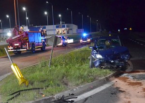Zdjęcie rozbitego opla, a w tle radiowóz z włączonymi światłami błyskowymi.