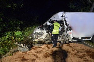 Policjant przeprowadza oględziny miejsca wypadku. W tle rozbity peugeot.
