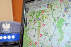 Krajowa Mapa Zagrożeń Bezpieczeństwa wyświetlona na ekranie monitora. Po lewej stronie monitora leży czapka policjanta w stopniu aspiranta sztabowego.