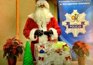 W lewej części kadru Mikołaj z brodą i w czerwonym stroju. Po prawej stronie zdjęcia rollup z logiem Komendy Powiatowej Policji w Starogardzie Gdańskim.