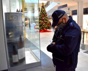Policjant wypisuje mandat karny. W tle świąteczny wystrój galerii.