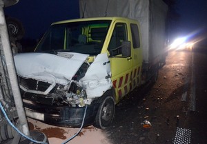Przód rozbitego volkswagena LT, a w oddali radiowóz z włączanymi światłami błyskowymi.