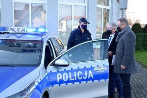 Zdjęcie z uroczystości przekazania nowego radiowozu na tle budynku Komendy Powiatowej Policji w Starogardzie Gdańskim. W prawej części kadru przedstawiciele samorządu, podczas uroczystości przekazania radiowozu. W lewej części kadru przekazywany radiowóz.
