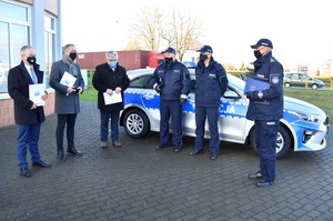 Zdjęcie z uroczystości przekazania nowego radiowozu na tle budynku Komendy Powiatowej Policji w Starogardzie Gdańskim. Na pierwszym planie przedstawiciele samorządu podczas uroczystości przekazania radiowozu. W tle przekazywany radiowóz.