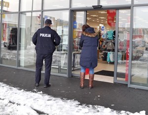 Policjant przed drzwiami prowadzącymi do sklepu sprawdza czy zamieszczone zostały informacje dla klientów.