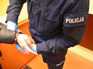 Umundurowany policjant zakłada zatrzymanemu kajdanki.