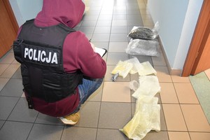Policjant w komendzie prowadzi oględziny rozłożonych na podłodze narkotyków.