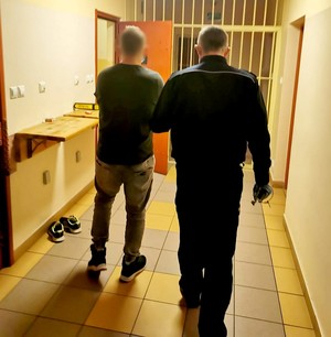 Policjant prowadzi zatrzymanego na przesłuchanie.