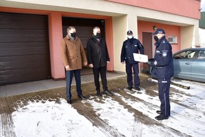 Komendant przemawia zwracając się do przedstawicieli lokalnego samorządu. W tle wymienione drzwi wjazdowe do garaży posterunku.