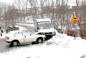 Droga w warunkach zimowych. W centralnej części kadru dwa auta bezpośrednio po zdarzeniu. Po prawej stronie widoczny znak drogowy ostrzegawczy &amp;quot;Uwaga śliska jezdnia&amp;quot;.