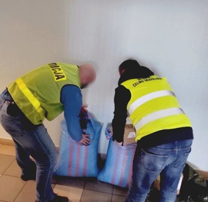 Policjant z funkcjonariuszem Krajowej Izby Celno-Skarbowej przenoszą worki z zabezpieczonym tytoniem.