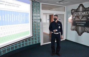 Policjant stoi przed ekranem rzutnika i omawia dane przedstawione na slajdzie.