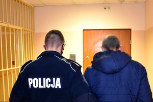 Policjant prowadzi zatrzymanego korytarzem komendy.