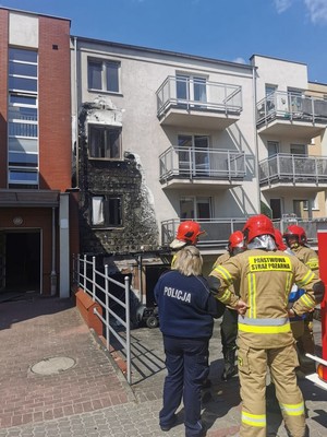 Policjantka rozmawia ze strażakami przy ugaszonym budynku.