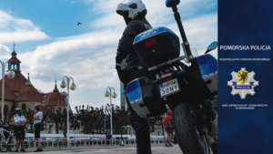 Policjant stoi przy motocyklu. W prawej części zdjęcia granatowy pas z logiem Komendy Wojewódzkiej Policji w Gdańsku.