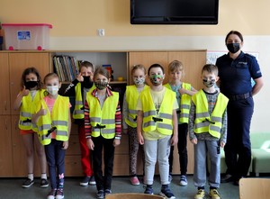 Zdjęcie grupowe. Policjantka stoi z grupą dzieci. Uczniowie mają założone kamizelki odblaskowe, które otrzymali od prowadzącej spotkanie policjantki.