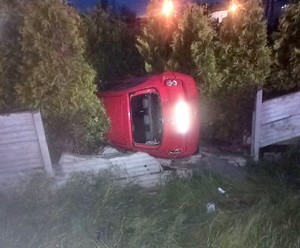 Leżący na lewym boku nissan, a po obu stronach zniszczone betonowe ogrodzenie.