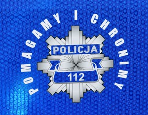 Gwiazda policyjna naklejana na drzwiach radiowozu. Wokół napis o treści:  Pomagamy i Chronimy.