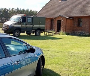 Na pierwszym planie po lewej stronie radiowóz policyjny. W oddali widać pojazd służbowy patrolu saperskiego.