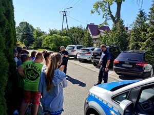 Policjanci rozmawiają w plenerze z uczniami o bezpiecznych zachowaniach w czasie wakacji.