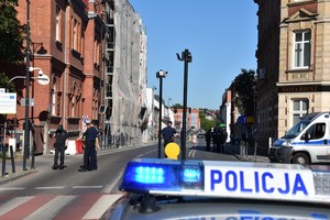Na pierwszym planie kogut radiowozu policyjnego. W oddali policjanci kierujący ruchem na ulicy Kościuszki.