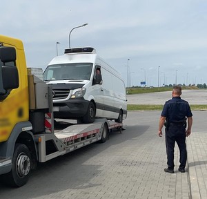 Odzyskany sprinter w trakcie załadunku na lawetę. W pobliżu stoi policjant, który nadzoruje załadunek.