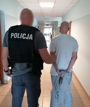 Policjant prowadzi podejrzanego na przesłuchanie.