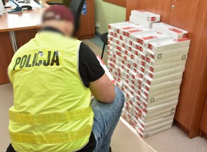 Policjant prowadzi w biurze oględziny zabezpieczonych papierosów.