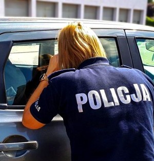 Policjantka zagląda do wnętrza zamkniętego samochodu.
