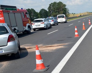 Ogólny widok na miejsce zdarzenia. Widoczne pojazdy służb ratowniczych i rozstawione na drodze pachołki.