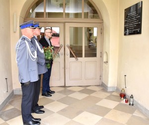 Policjanci z proboszczem parafii oddają hołd przed tablicą zamordowanych policjantów.