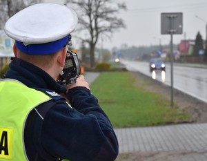 Policjant z miernikiem prędkości stoi przy drodze i mierzy prędkość nadjeżdżających pojazdów.