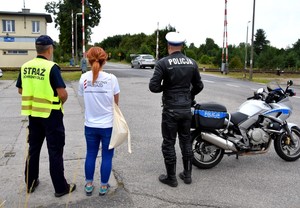 Uczestniczy kampanii, policjant i przedstawiciele PKP obserwują ruch na przejeździe kolejowym.