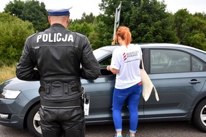 Przedstawicielka PKP wraz z policjantem wręczają ulotki informacyjne kierowcy auta osobowego.