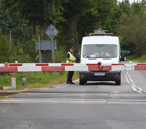 Pracownik PKP wręcza ulotki informacyjne kierowcy auta stojącego przed przejazdem kolejowym.
