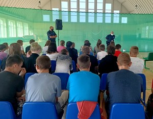 Policjanci na sali sportowej rozmawiają z młodzieżą szkolną.