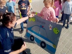 Policjantka odbiera plakat z namalowanym radiowozem z podziękowaniem za przeprowadzenie pogadanki.