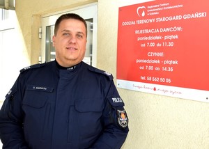 Policjant przy tablicy informacyjnej starogardzkiego punktu krwiodawstwa.
