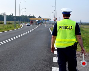 Policjant w żółtej kamizelce odblaskowej z lizakiem w ręku stoi przy bramkach autostrady A1.