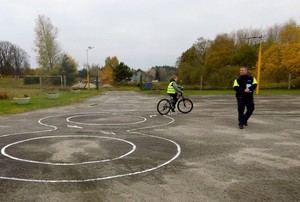Policjant na placu manewrowym przygląda się umiejętnościom egzaminowanego rowerzysty.