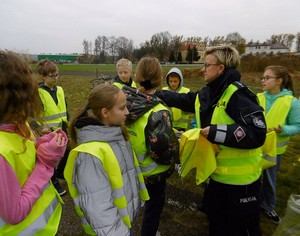 Policjantka rozdaje kamizelki odblaskowe.