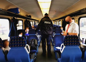 Policjanci kontrolują czy pasażerowie pociągu mają zasłonięte usta i nos w czasie podróży.