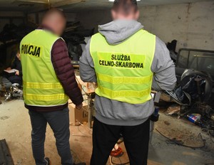 Funkcjonariusz policji oraz urzędu celno-skarbowego stoją przy urządzeniu służącym do nielegalnej produkcji papierosów.